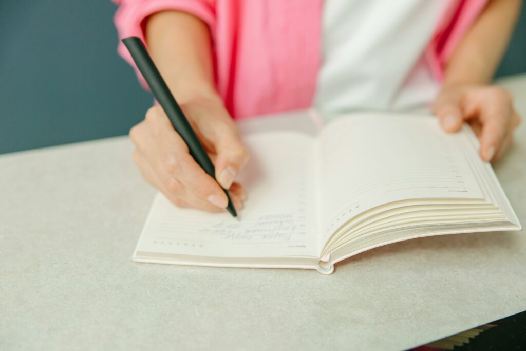 Personne en chemise rose écrivant sur le cahier blanc